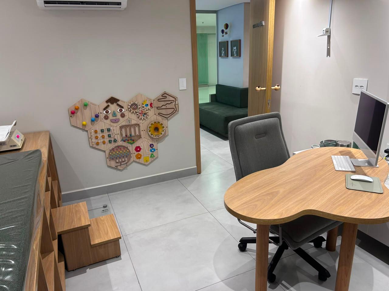 Consultório pediátrico com painel sensorial de madeira e escada infantil ao lado da maca