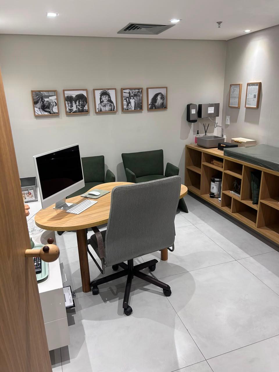 Sala de atendimento da Dra. Ana Maria Lorga com mesa de madeira, poltronas verdes e maca pediátrica